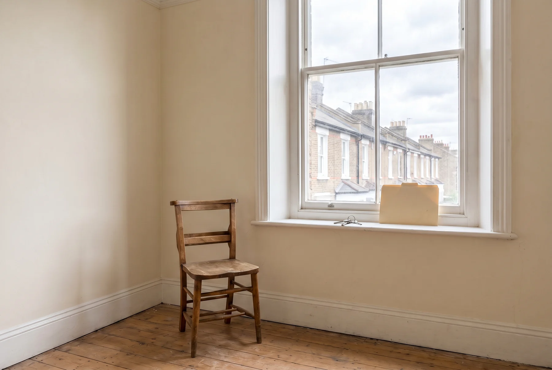 An empty, freshly cleaned flat between tenancies, with a wooden chair, bare floorboards and a set of keys and a folder on the windowsill overlooking a London terrace