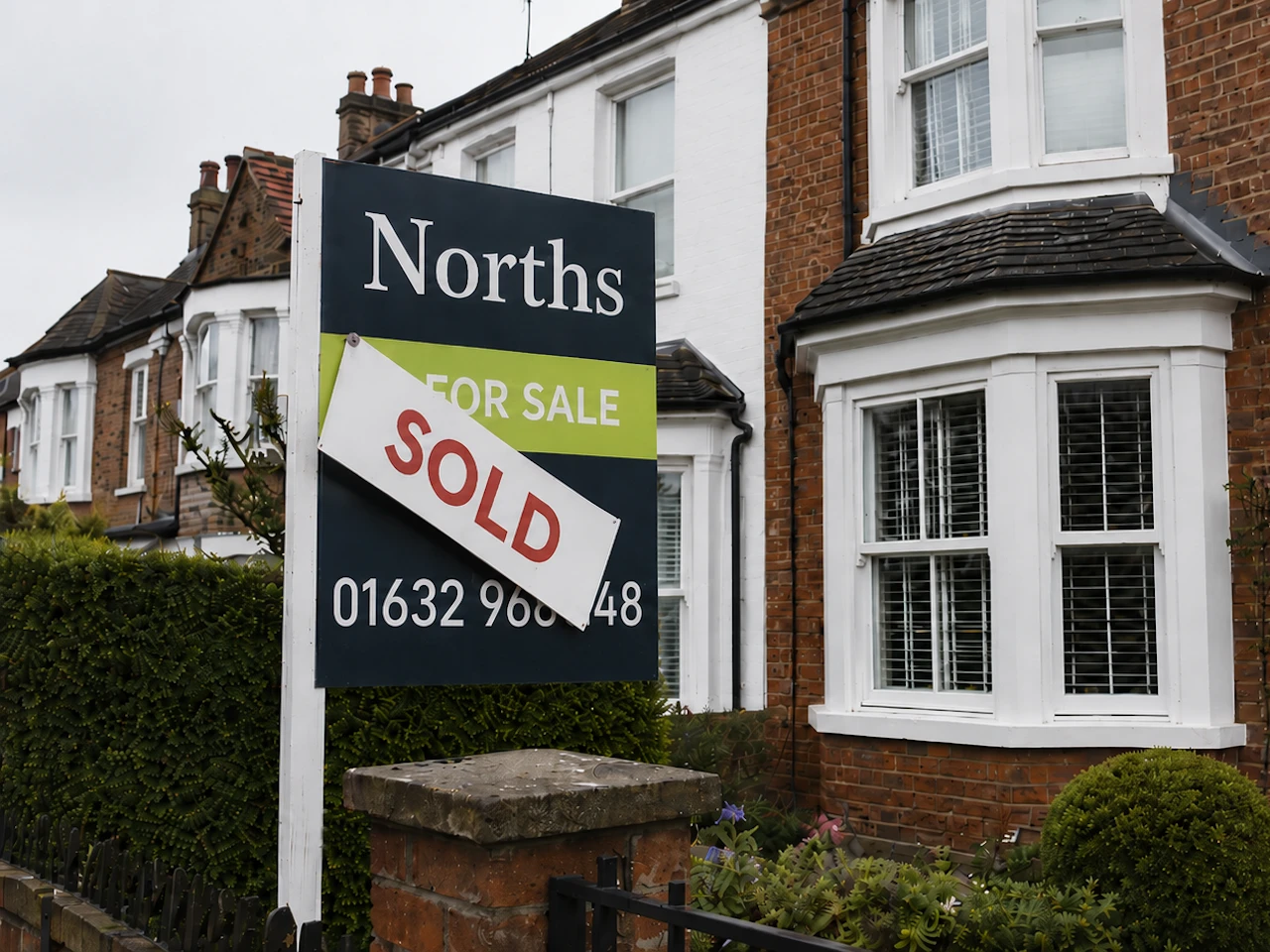 An estate agent For Sale board with the SOLD slip slipping off at an angle, outside a Victorian terraced street, suggesting a property sale that has fallen through