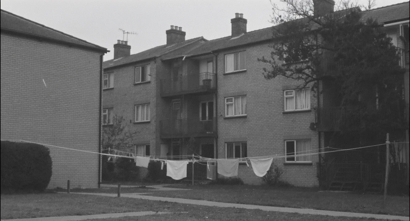 A vintage 1950s black-and-white photograph of low-rise brick council flats with balcony access and washing lines strung across a communal yard
