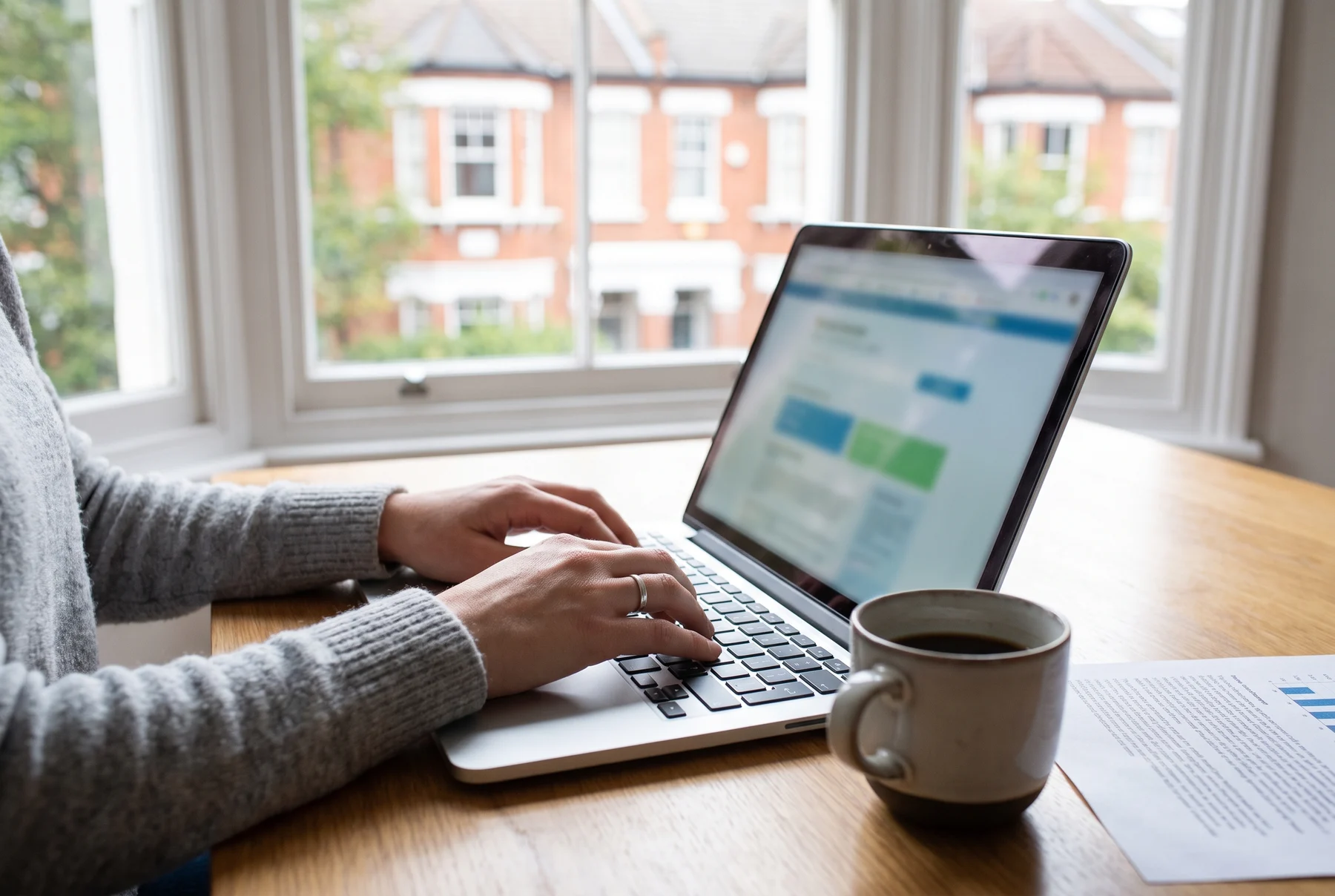 Checking a lease online at a kitchen table: hands on a laptop, a printed title register and a row of London houses through the window