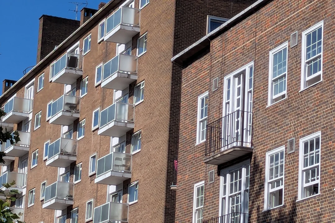 Balconies and white sash windows on a brick block of London flats under a blue sky