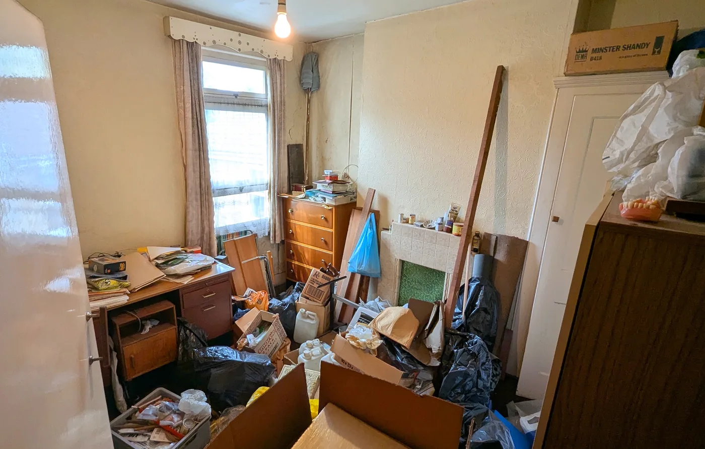 A cluttered room in a run-down flat, filled with boxes, bags and old furniture
