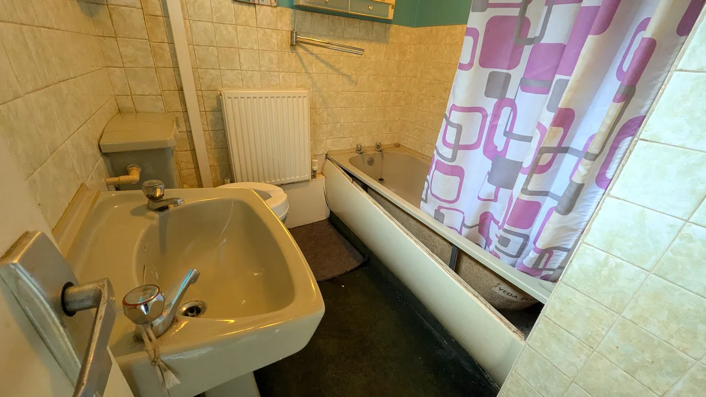 A dated bathroom with an old coloured suite, beige wall tiles and worn flooring