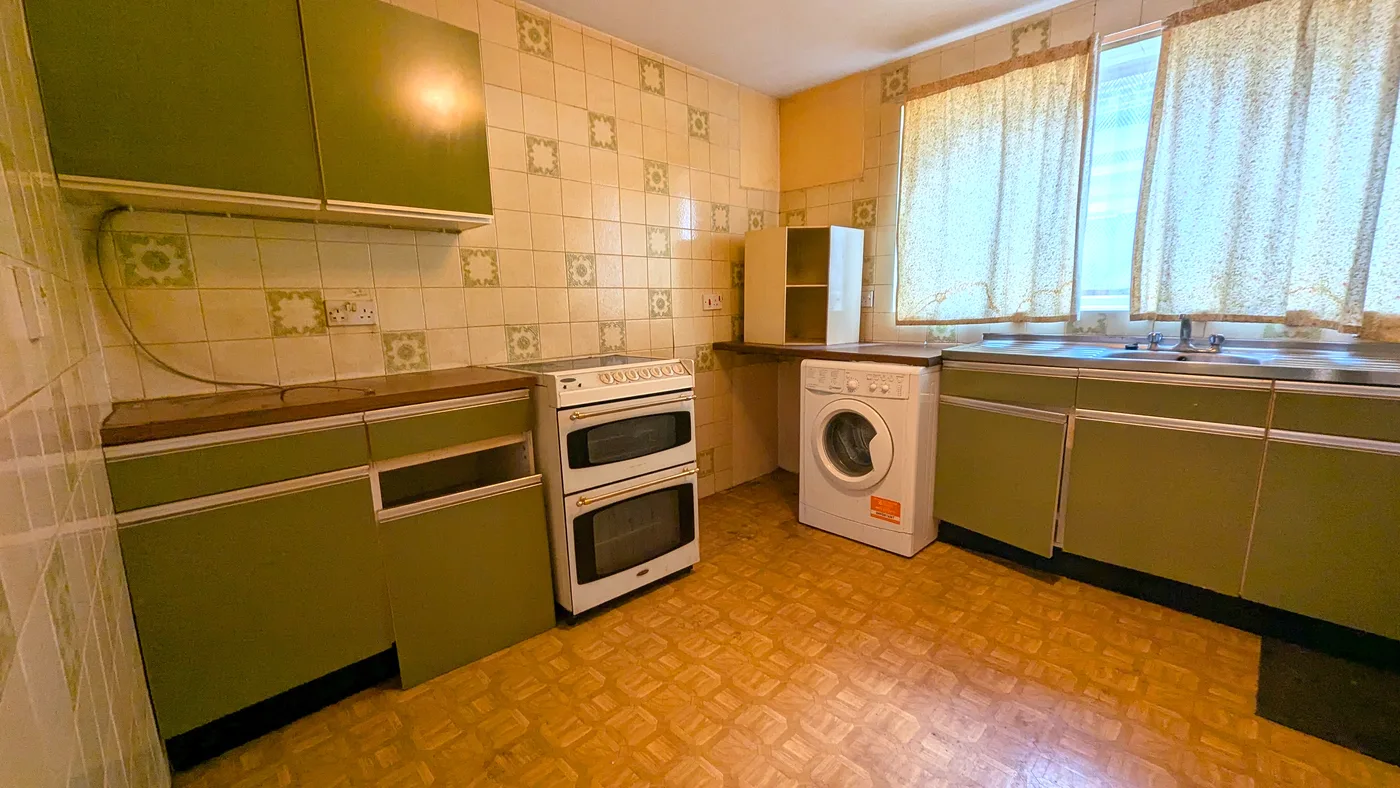 A dated but functional kitchen with olive-green units and patterned wall tiles, cosmetically tired rather than derelict