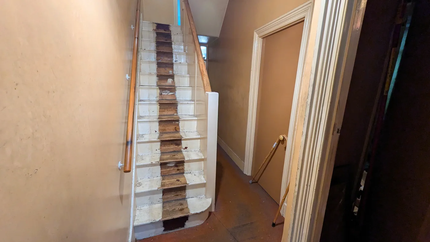 A staircase in a run-down flat with the carpet stripped back to bare treads