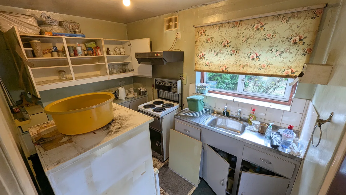 A worn kitchen with damaged worktops, missing cupboard doors and dated fittings