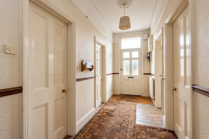 Communal entrance hall of a Victorian house converted into flats, with woodchip wallpaper, a patterned carpet runner, a post shelf and three flat doors