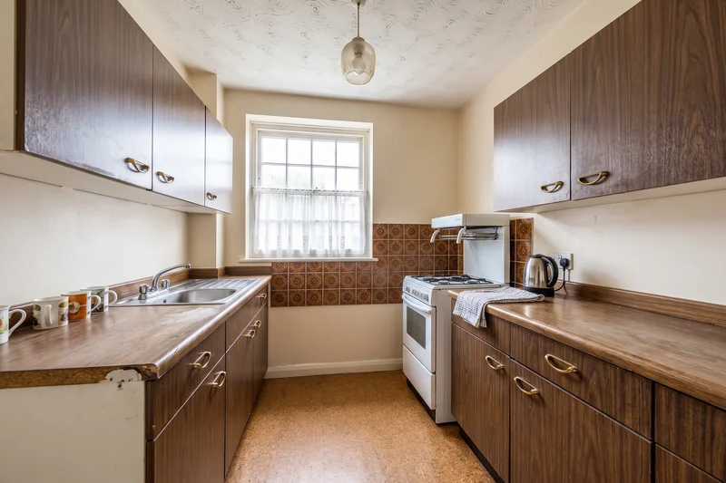 Unmodernised 1970s kitchen in a London flat with wood-effect units, patterned tiles and a freestanding cooker