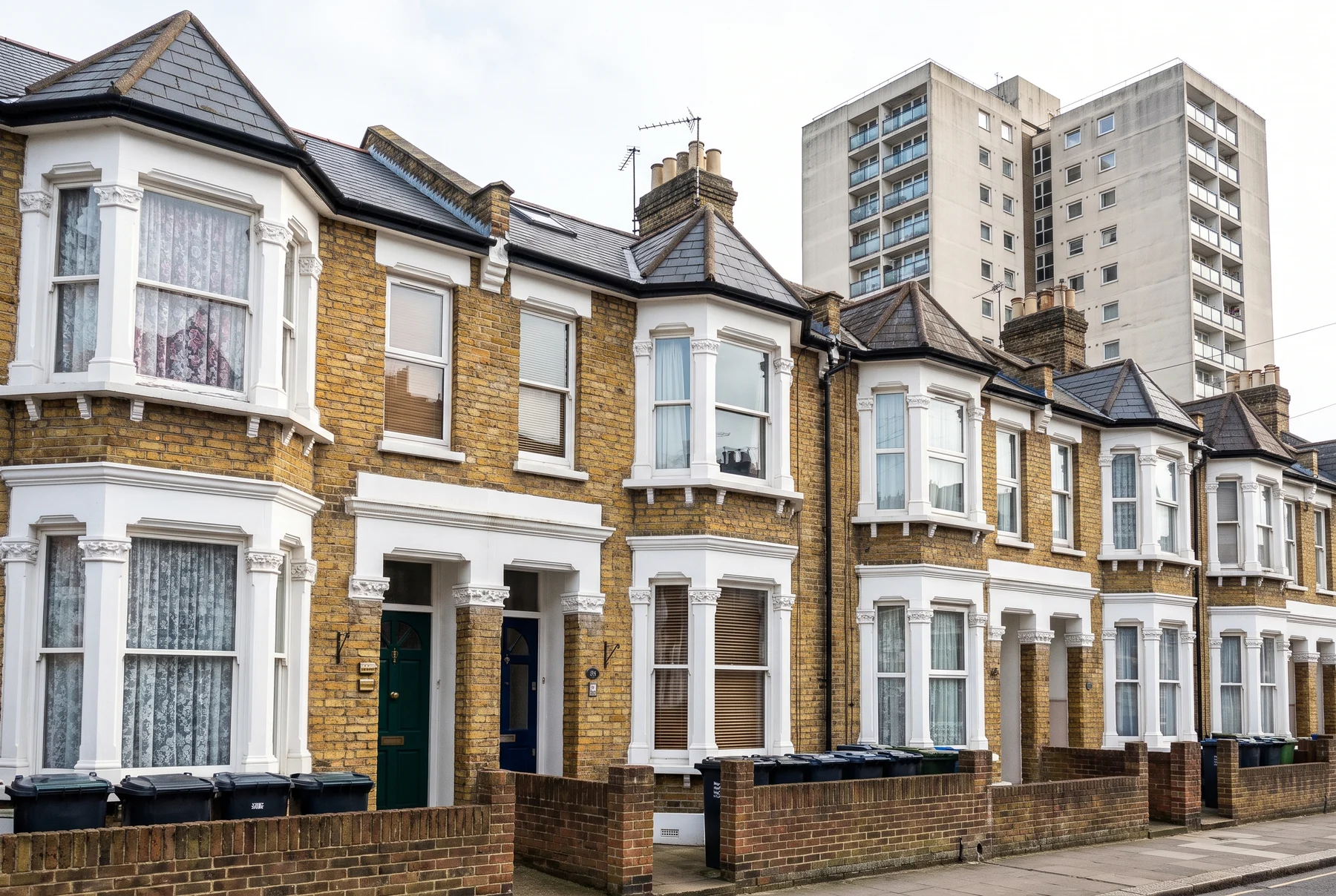 A row of Victorian terraced houses converted into flats, with two council tower blocks rising behind them